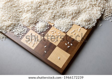 A wooden chessboard with one grain of rice on the first square, doubling at each square. The tale of the king and chess master illustrates the concept of exponential growth and geometric series. Royalty-Free Stock Photo #1966172239