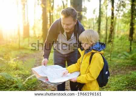 Schoolchild and his mature father hiking together and exploring nature. Little boy with dad looking map during orienteering in forest. Adventure, scouting and hiking tourism for kids. Daddy and son Royalty-Free Stock Photo #1966196161