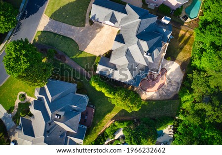 Top down view of beautiful houses, roofs and lush green landscaped yards in an upscale subdivision in suburbs of USA shot during Golden hour during early spring.
