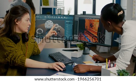 Gamer creator explaning to african worker how testing game level interface, developing new design in creative office using pc with two monitors. Player online video games with technology network