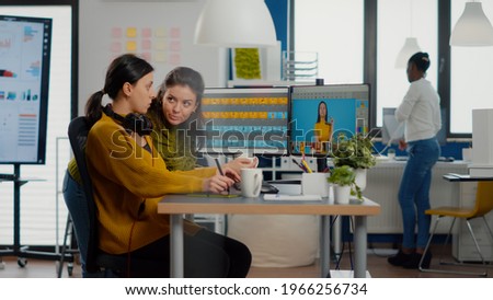 Confident women photo editors sitting at workplace in creative studio retouching photo, art director explaning color greding technic. Retouchers editing with drawing tablet and stylus pencil