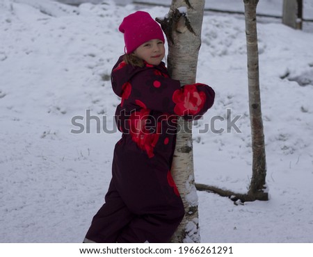 Portrait of a beautiful girl in a red cap, hugging a birch tree.