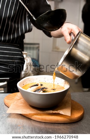 The cook pours the liquid from the pot into the soup. Cooking dinner. Kitchen on the background