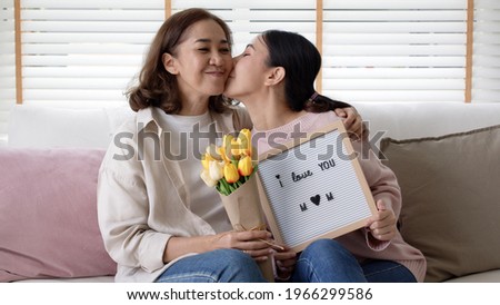Portrait attractive beautiful mum sit with daughter give gift photo frame and flower in family moment celebrate look at camera. Overjoy bonding cheerful kid embrace relationship with retired mom.