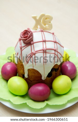 Easter cake decorated with the letters X and B, which means Christ is Risen, with pink and green eggs around.


