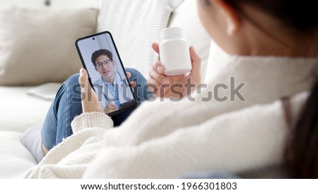 Over shoulder view of young asia woman talk to doctor on cellphone videocall conference medical app in telehealth telemedicine online service hospital quarantine social distance at home concept. Royalty-Free Stock Photo #1966301803