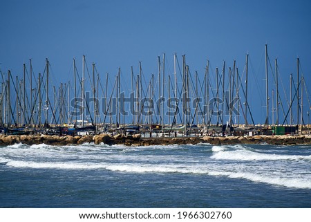                             Horizontal view of sailing boat masts against blue sky background on a sunny day and the sea waves in front. Picture was taken on a Tel-Aviv port.