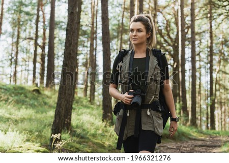 Woman hiker walking with a backpack and modern mirrorless camera in green forest