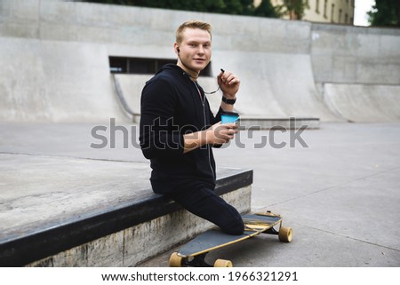 Young and motivated handicapped guy with a cup of coffee before longboard riding in a skatepark