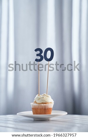 Digital gift card concept. Tasty homemade vanilla anniversary or birthday cupcake with creamy topping and number 30 thirty with bright background in minimalistic style. High quality vertical image