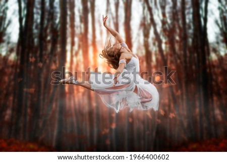 Flying attraction of a young beautiful ballerina. Attractive model in ballerine dress jumping up in the forest. Dark blurry background with sunset