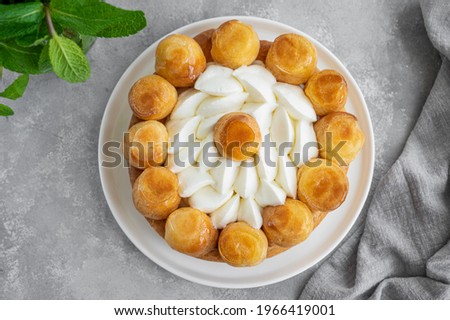 Saint Honore cake with profitrols, caramel, custard and whipped cream on a white plate on a gray concrete background. Traditional French dessert. Copy space Royalty-Free Stock Photo #1966419001