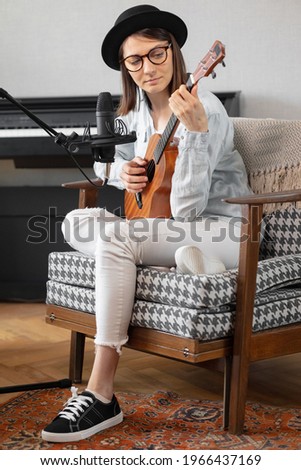 podcast, music audio content creation. beautiful European woman podcaster in a hat with a guitar or ukulele, radio host recording podcast or content