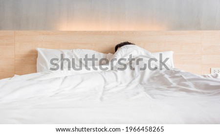 Man sleeping on the bed in white blanket at lately morning, laziness concept