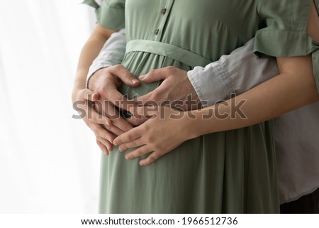 Crop close up of happy future multiracial parents touch hold baby bump excited to meet kid child. Diverse man and woman couple caress belly, enjoy pregnancy. Family, parenthood concept. Royalty-Free Stock Photo #1966512736