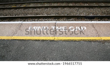 A painted floor sign on the railway platform, advising passengers to mind the gap