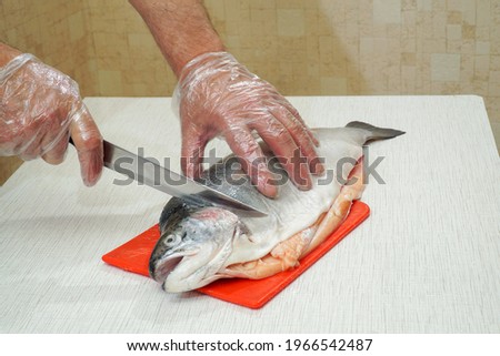 On the table, on a cutting board, lies a gutted fish from the salmon trout family, which the chef begins to cut into pieces.                               