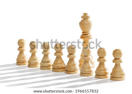 The king stands behind a row of white pawns on a white background with a long shadow. White wooden chess pieces, closeup.