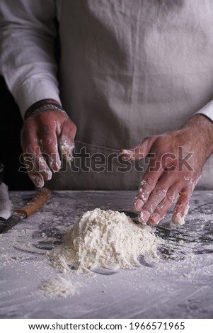 A male chef cook in a white shirt and grey apron making dough