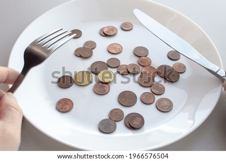 Pile of euro coins lie on a plate. Male hands hold cutlery knife and fork to start eating a dish. View from above. Concept of eating up money, wasting, spending, buying food.