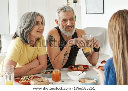 Happy mature family couple having breakfast with teen daughter sit at kitchen table. Smiling older mid age parents having fun talking, eating toasts and waffles enjoying morning meal together.