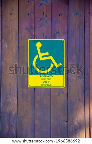 A green-yellow plastic sign for the toilet of a wheelchair user with the indication in several languages that it is for wheelchair users only