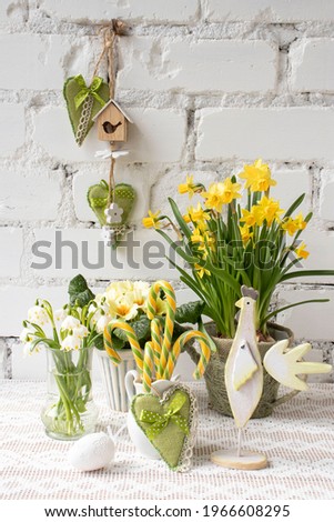 Spring Easter still life with flowers, candy in the form of a cane, decorative eggs against a white brick wall.
