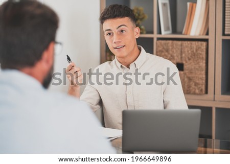 Portrait of teenager man smiling and talking to a man next to her talking about business work together in the office. Businessman working from home indoor. Royalty-Free Stock Photo #1966649896