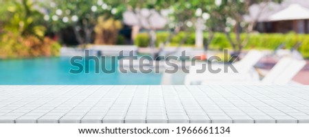 Empty white ceramic mosaic table top and blurred swimming pool in tropical resort in summer banner background - can used for display or montage your products. Royalty-Free Stock Photo #1966661134