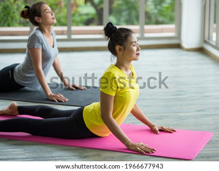 Two Asian sportive healthy woman with hair tied wearing sport shirt and black elastic pants, doing exercise, yoga, stretching her back and body while lying down on mat at home