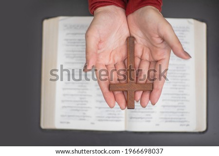 Woman hands praying with a bible and wooden cross.