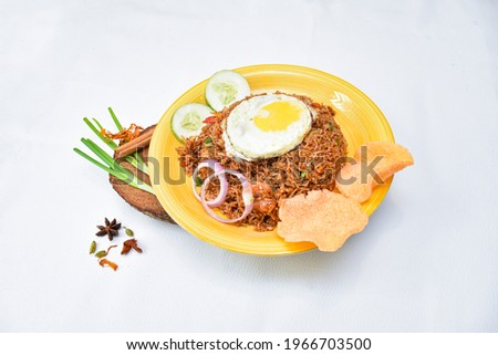 Nasi Goreng - Indonesian Chicken Fried Rice on a yellow plate on the white color backdrop. Nasi Goreng is an Indonesian cuisine dish with jasmine rice, chicken meat, onion, egg, vegetables. Indonesian