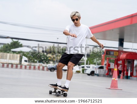 Asian young man skater riding on skateboard on courtyard at gas station with wear sunglasses. Young man teenager skateboarding outdoor