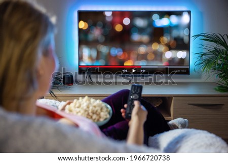 Woman relaxing at home in evening and watching TV Royalty-Free Stock Photo #1966720738