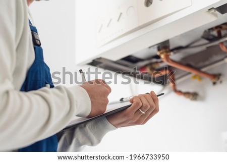Professional plumber checking a boiler at home and writing on a clipboard Royalty-Free Stock Photo #1966733950