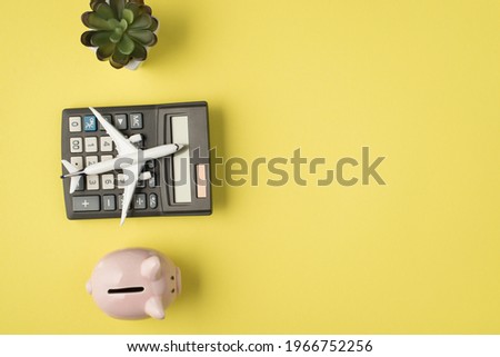 Top view photo of flowerpot plane model on calculator and piggy bank on isolated pastel yellow background with copyspace