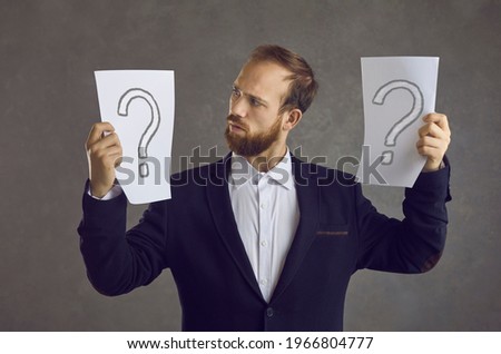 Don't know which to choose. Man holding two sheets of paper with question mark symbols, thinking, unsure, trying to make choice between different business options, asking himself what decision to take