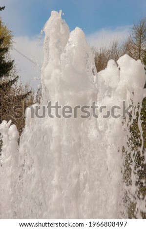 A shapeless stream of foam with many bubbles and splashes, shooting up against the blue sky with clouds. Close up.