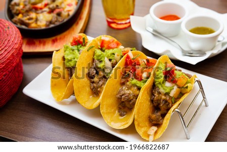 Traditional Mexican tacos with juicy roasted beef, guacamole, fresh vegetables and sauces..