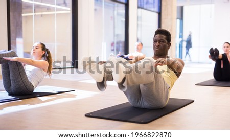 Portrait of young adult man making pilates exercises with group in yoga studio