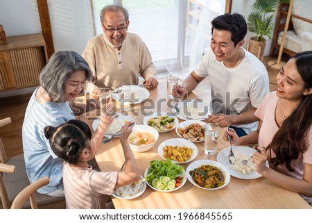 Big Asian happy family spend time having lunch on dinner table together. little kid daughter enjoy eating food with father, mother and grandparents. Multi-Generation relationship and activity in house Royalty-Free Stock Photo #1966845565