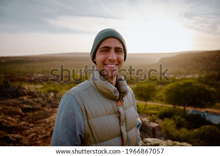 Portrait of cheerful young male hiker looking satisfied after reaching cliff of mountain looking at camera Royalty-Free Stock Photo #1966867057