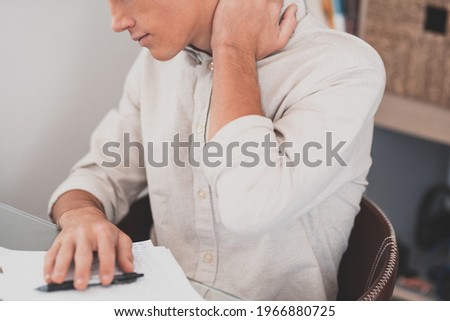Close up rear view stressed young man touching lower neck feeling discomfort, suffering from sudden pain due to sedentary lifestyle or long computer overwork in incorrect posture at home office. Royalty-Free Stock Photo #1966880725