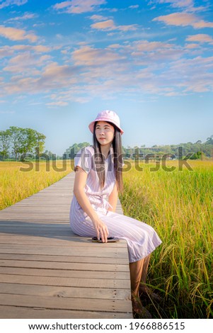 Asian girl dressed in pink sitting on wooden bridge with Thai fields