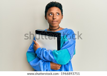 Young african american girl holding books smiling looking to the side and staring away thinking. 
