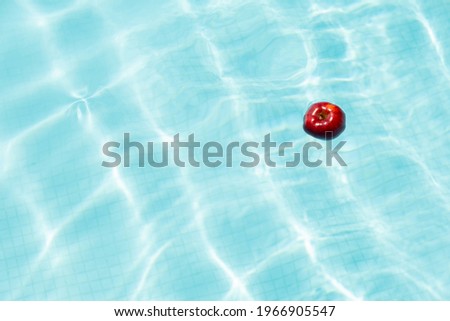 Red apple floating in the blue water pool with copy space background texture for background or backdrop.
