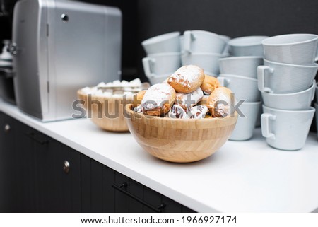 On the table is a bowl of cookies, a coffee machine and clean white mugs. Cookies for breakfast, coffee break. Office interior