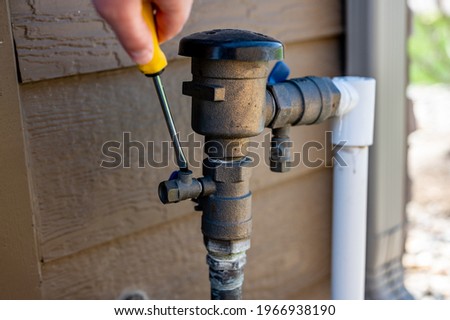 Using a flathead screwdriver to close the test cock next to the vacuum breaker to startup a sprinkler irrigation system in the spring Royalty-Free Stock Photo #1966938190