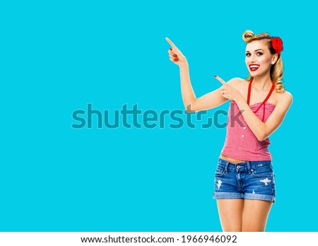 Amazed happy woman pointing at something. Excited girl in pin up, showing advertising product or copy space for ad text. Retro fashion and vintage. Isolated over aqua blue color background.