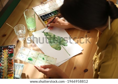 Young woman drawing leaf with watercolors at table, closeup Royalty-Free Stock Photo #1966958812